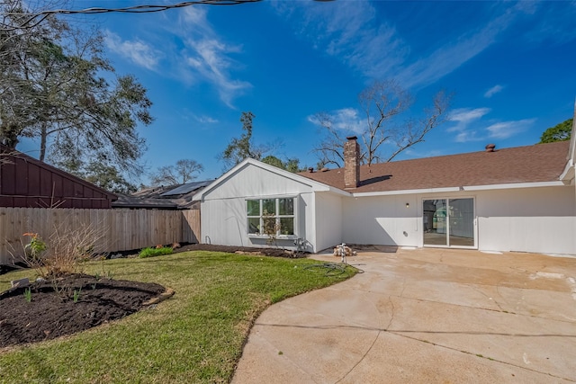 back of property featuring a patio, a yard, a chimney, a shingled roof, and fence