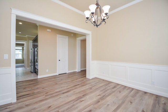 empty room with ornamental molding, wainscoting, an inviting chandelier, and light wood-style floors