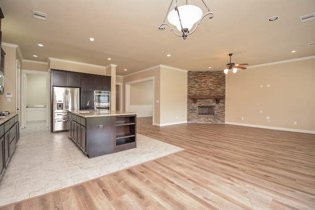 kitchen featuring light wood-style flooring, stainless steel appliances, a fireplace, visible vents, and an island with sink