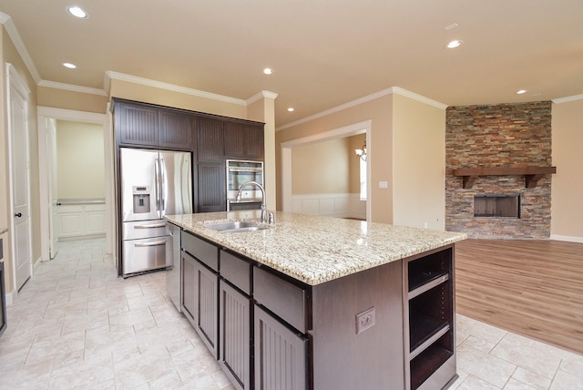 kitchen with appliances with stainless steel finishes, dark brown cabinets, a sink, and a stone fireplace