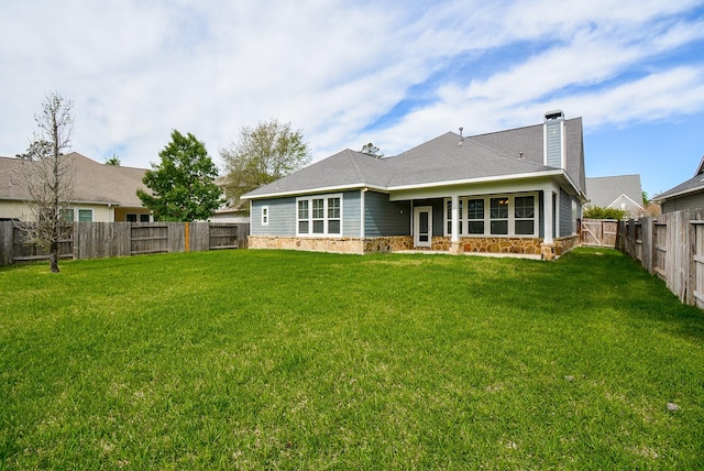 back of house featuring stone siding, a fenced backyard, a yard, and a chimney