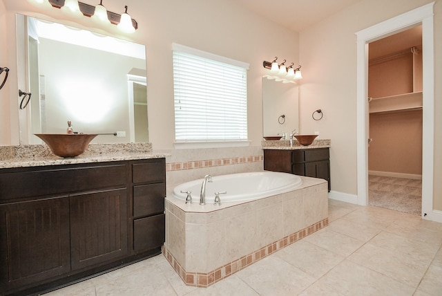 full bathroom with a walk in closet, a garden tub, two vanities, a sink, and tile patterned floors