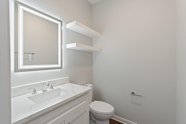 bathroom with toilet, a textured wall, vanity, and baseboards