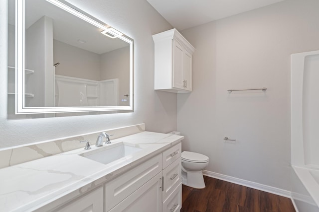 bathroom featuring toilet, vanity, wood finished floors, baseboards, and walk in shower