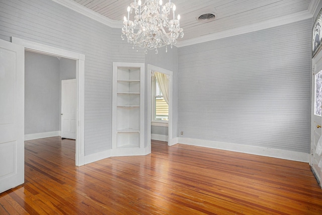 unfurnished room with baseboards, wood-type flooring, an inviting chandelier, crown molding, and built in shelves