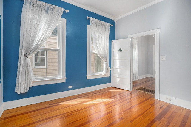 unfurnished room featuring ornamental molding, a wealth of natural light, baseboards, and hardwood / wood-style floors