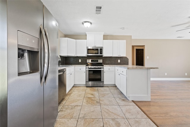 kitchen with baseboards, a peninsula, stainless steel appliances, white cabinetry, and backsplash