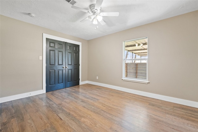 unfurnished bedroom featuring visible vents, a textured ceiling, wood finished floors, baseboards, and ceiling fan