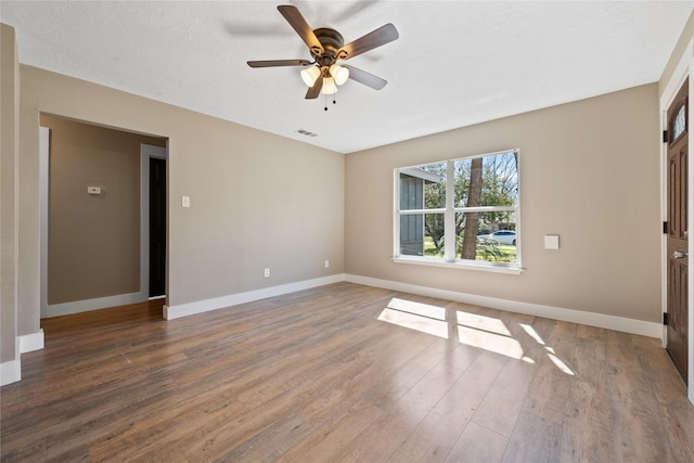 spare room with a ceiling fan, visible vents, wood finished floors, and baseboards