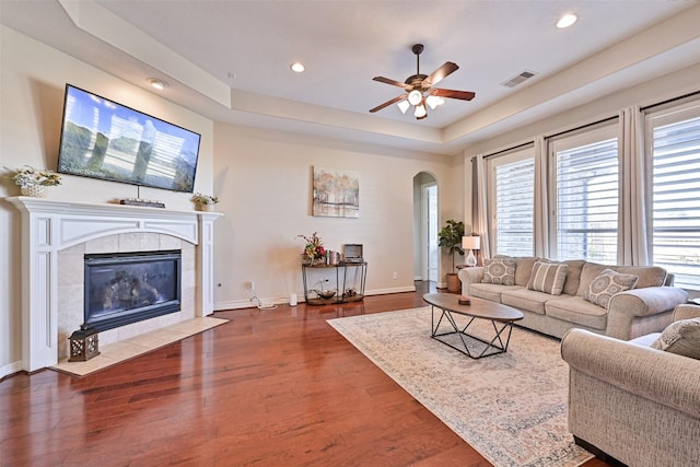 living room featuring visible vents, arched walkways, wood finished floors, a tray ceiling, and a fireplace