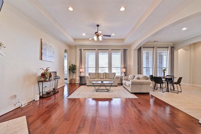 living area featuring arched walkways, a tray ceiling, recessed lighting, wood-type flooring, and baseboards