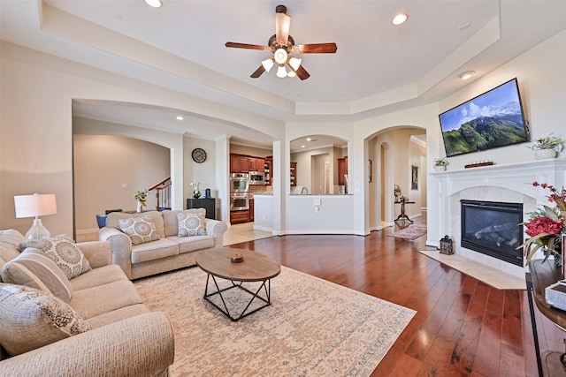 living room featuring a tile fireplace, recessed lighting, baseboards, dark wood-style floors, and a tray ceiling