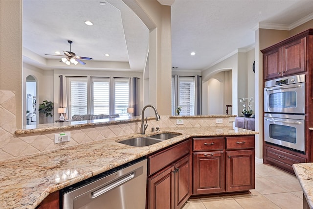 kitchen featuring light stone counters, stainless steel appliances, a sink, backsplash, and a tray ceiling