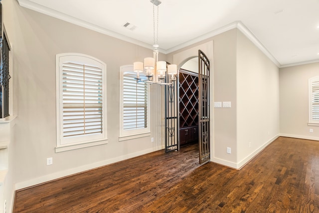 unfurnished dining area with baseboards, visible vents, wood finished floors, crown molding, and a chandelier