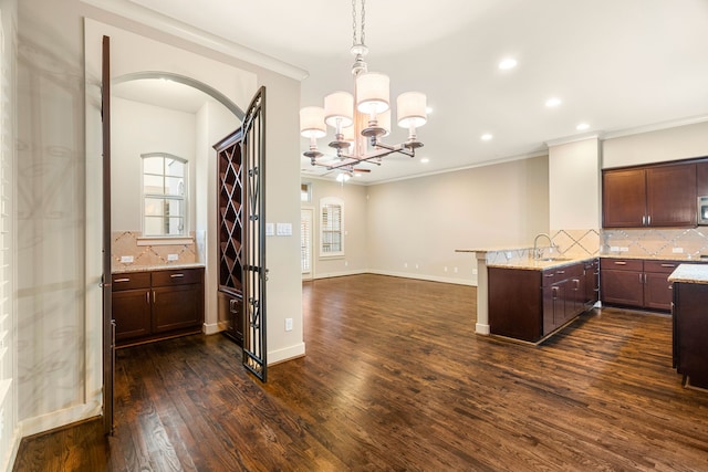 kitchen with arched walkways, a peninsula, dark wood-type flooring, decorative backsplash, and light stone countertops