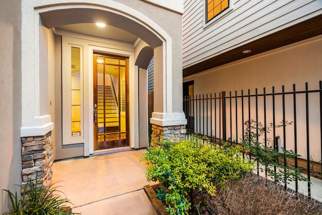 entrance to property with stone siding, fence, and stucco siding