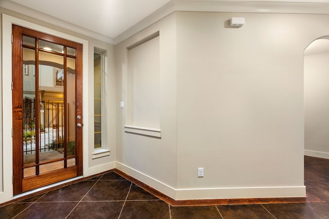 foyer entrance featuring arched walkways, crown molding, dark tile patterned floors, and baseboards