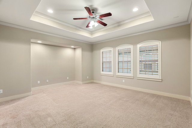 carpeted spare room featuring a tray ceiling, a ceiling fan, and baseboards