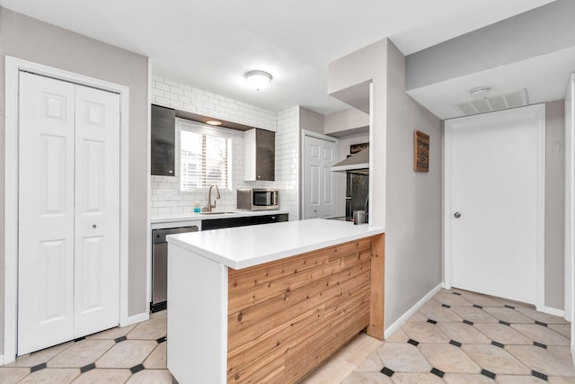 kitchen featuring appliances with stainless steel finishes, a sink, light countertops, light floors, and backsplash