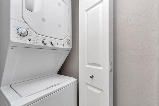 clothes washing area with stacked washer and dryer, laundry area, and a textured wall