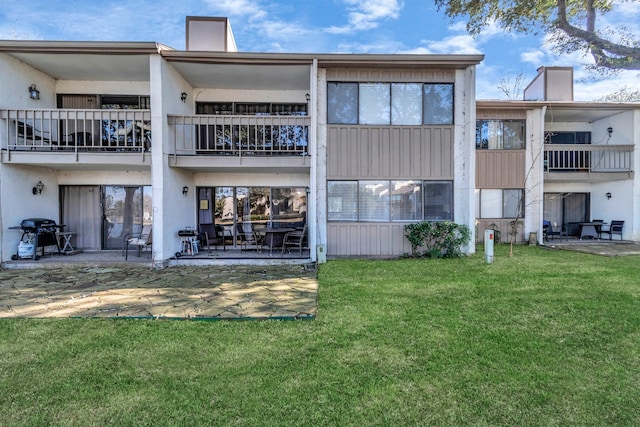 rear view of house with a lawn, a balcony, a chimney, a patio area, and stucco siding