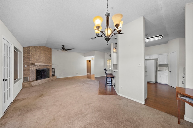 unfurnished living room featuring ceiling fan with notable chandelier, visible vents, vaulted ceiling, a brick fireplace, and dark carpet