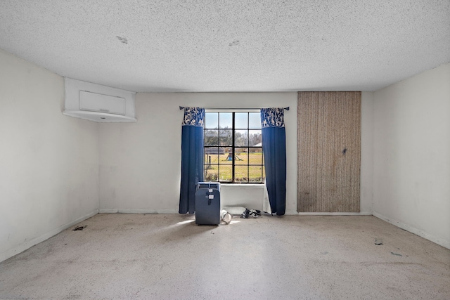 empty room featuring a textured ceiling, speckled floor, and baseboards