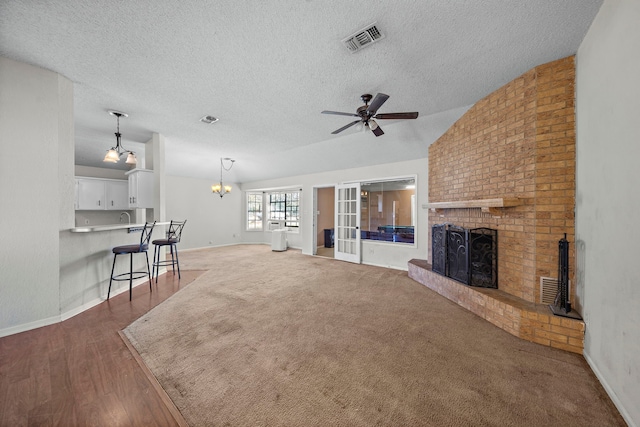 unfurnished living room with ceiling fan, a textured ceiling, visible vents, vaulted ceiling, and a brick fireplace