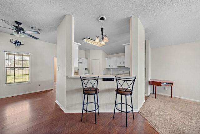 kitchen with a breakfast bar area, white cabinetry, wood finished floors, white appliances, and a peninsula