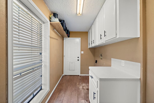 laundry area with cabinet space, a textured ceiling, baseboards, and wood finished floors