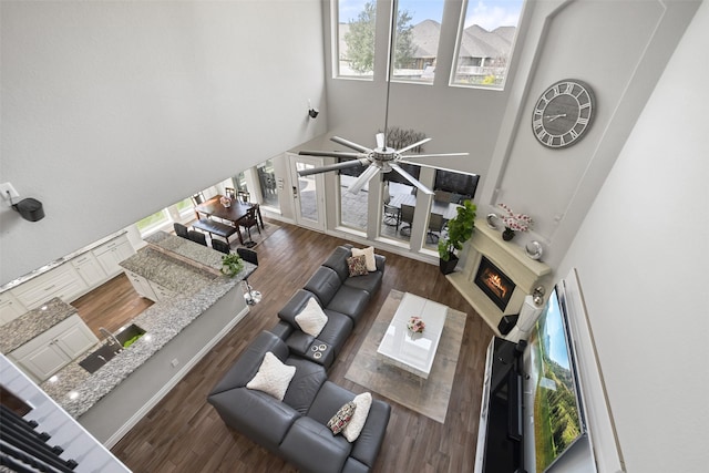 living room with a towering ceiling, a warm lit fireplace, and wood finished floors