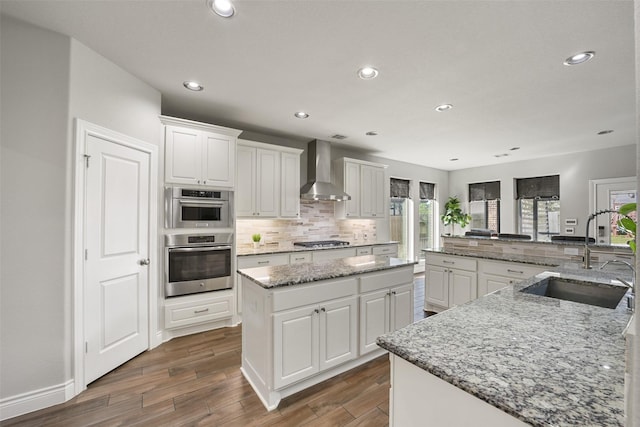 kitchen with a large island, stainless steel appliances, decorative backsplash, a sink, and wall chimney range hood