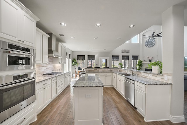 kitchen featuring stainless steel appliances, visible vents, decorative backsplash, a sink, and wall chimney range hood