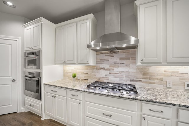 kitchen featuring dark wood finished floors, white cabinets, appliances with stainless steel finishes, wall chimney range hood, and backsplash