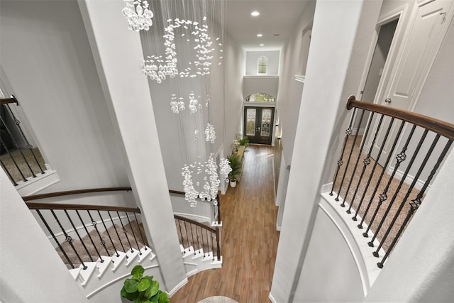 corridor with wood finished floors, stairway, french doors, and an inviting chandelier