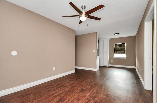 empty room with a ceiling fan, baseboards, and dark wood-type flooring