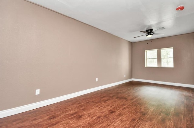 unfurnished room featuring dark wood-style flooring, a ceiling fan, and baseboards