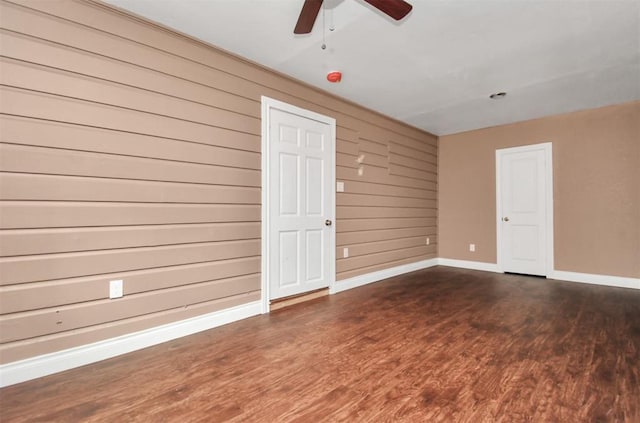 unfurnished room with wooden walls, baseboards, dark wood finished floors, and a ceiling fan