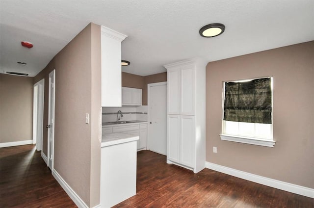 kitchen with dark wood-style flooring, white cabinets, a sink, and baseboards