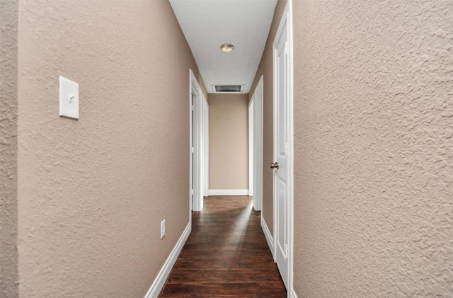 corridor with dark wood-style flooring, visible vents, a textured wall, and baseboards