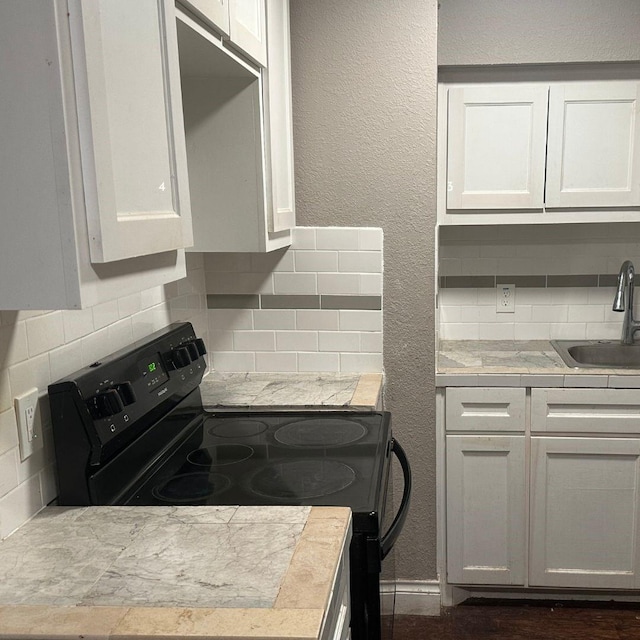 kitchen with black range with electric cooktop, decorative backsplash, white cabinets, and a sink