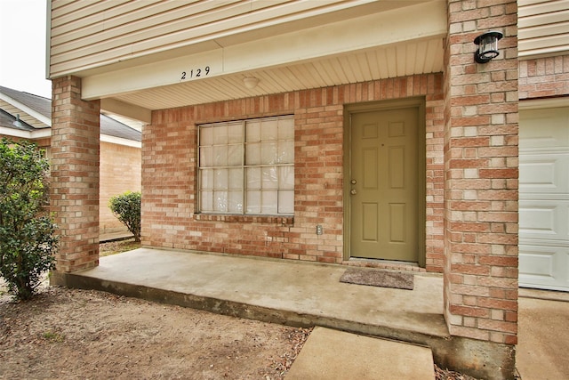 entrance to property featuring a garage and brick siding