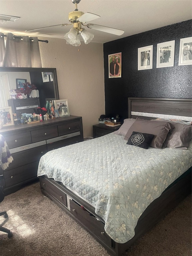 carpeted bedroom with a textured wall, visible vents, and a ceiling fan