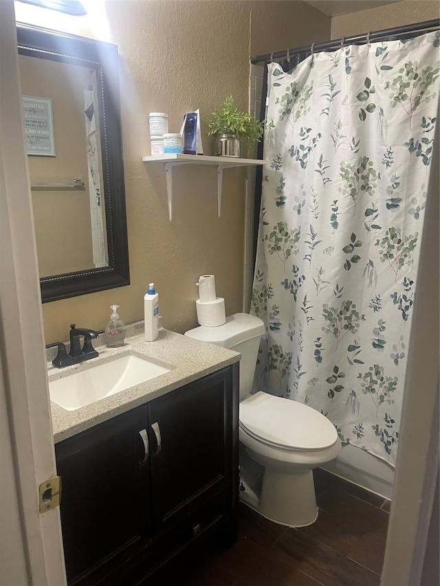 bathroom with a textured wall, toilet, and vanity