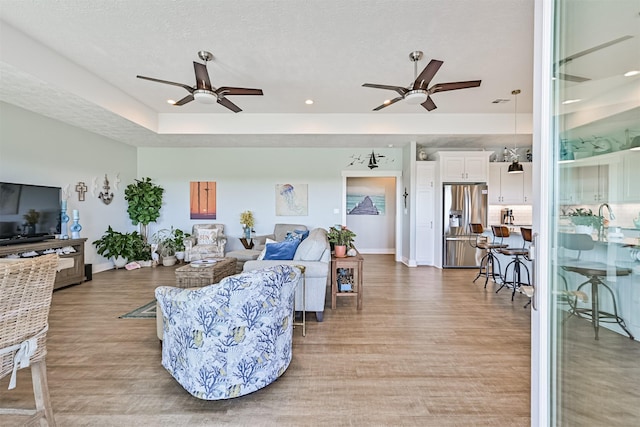 living room with light wood-style floors, a textured ceiling, baseboards, and a ceiling fan