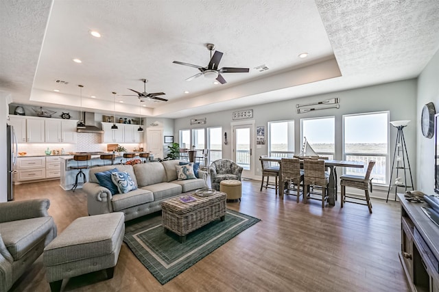 living room with visible vents, a raised ceiling, wood finished floors, a textured ceiling, and recessed lighting