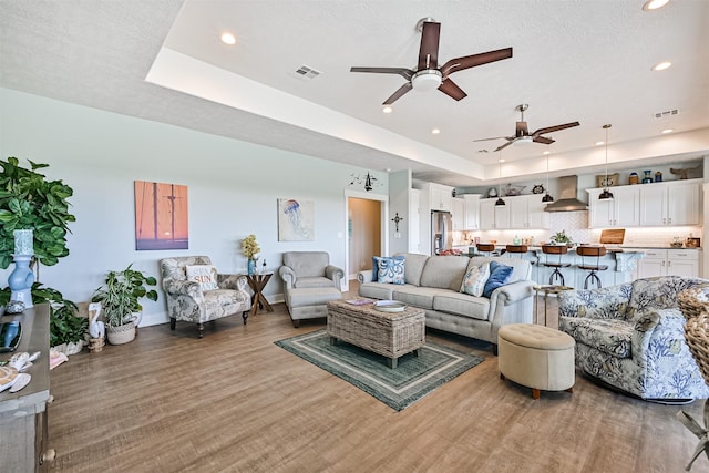 living room with a tray ceiling, visible vents, a textured ceiling, and wood finished floors