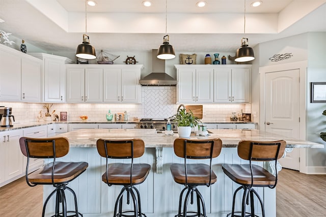 kitchen featuring wall chimney exhaust hood, stove, light wood-style floors, a kitchen bar, and white cabinetry