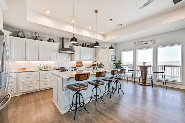 kitchen featuring wall chimney exhaust hood, freestanding refrigerator, a raised ceiling, and visible vents