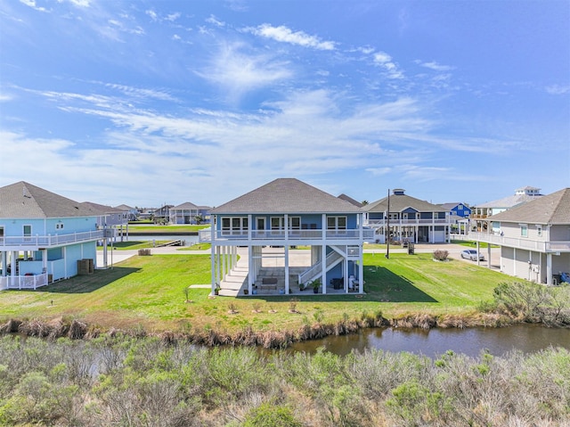 rear view of house featuring a water view, stairs, a residential view, and a lawn